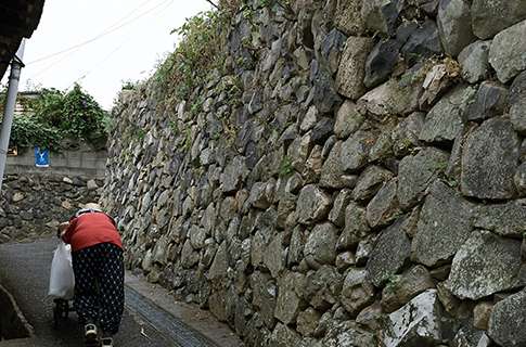 男木島の路地をオンバを押してのぼる女性