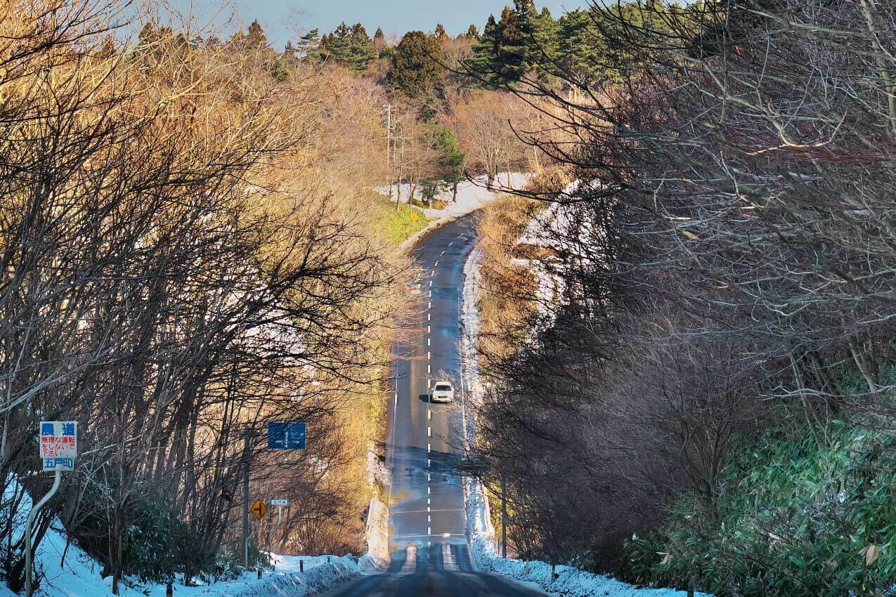 青森県 十和田の雪が残る坂道を走るレヴォーグ(クリスタルホワイトパール) | SUBARU グランドツーリングNIPPON
