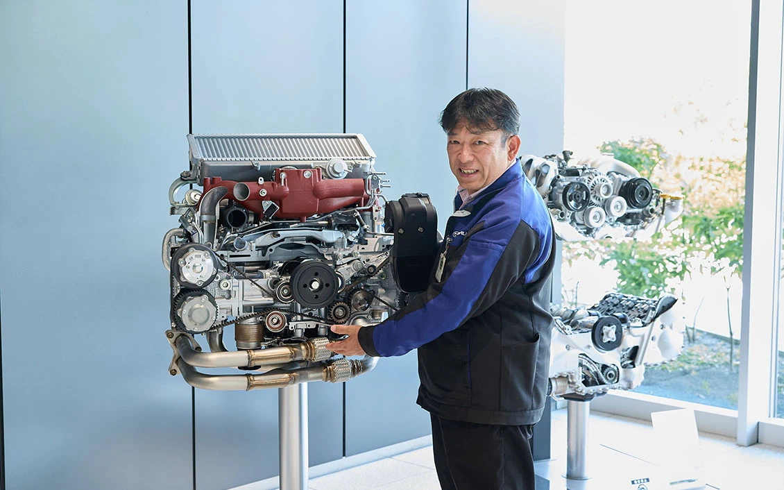 EJ20のエンジン模型と一緒に映る関さん