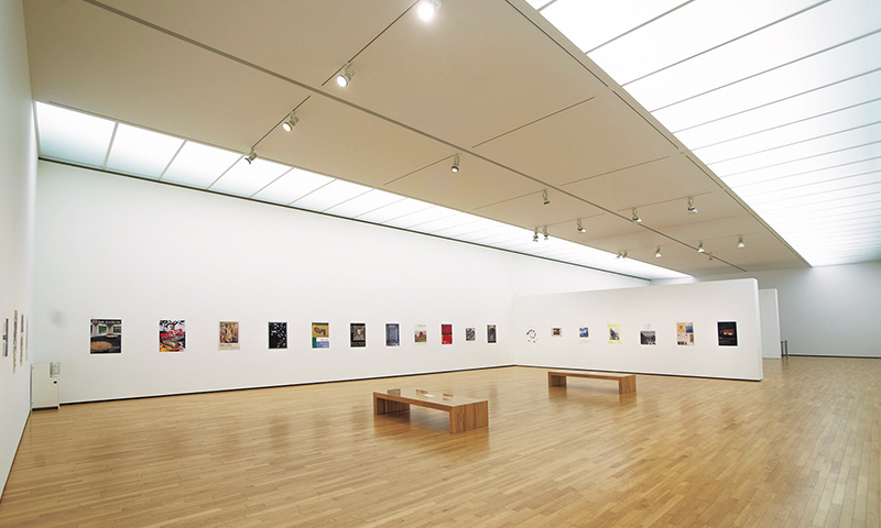 天井が高く、柔らかな間接照明が作品を照らし出す展示室。取材日は過去の展覧会のポスターを展示。