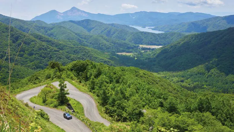 カートピア 西吾妻スカイバレーを登っているフォレスター。遠くには山々が広がり、左奥には磐梯山が見える | SUBARU