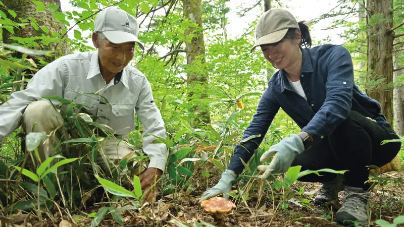 カートピア 森の中で地面に自生しているキノコを見つけ、笑顔の藤島さんと古畑さん | SUBARU