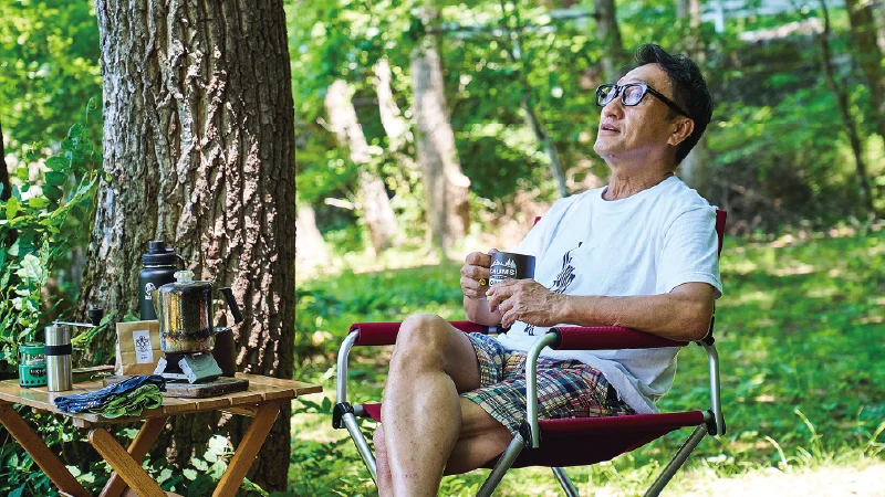 カートピア コーヒーを片手にキャンプチェアに腰掛ける酒井直人 | SUBARU