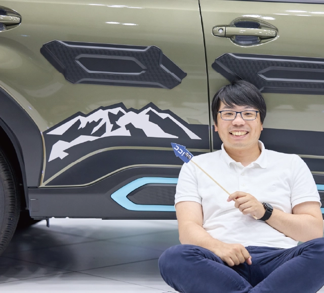 カートピア ココスバポインターで新型フォレスターのボディ右側面に装着されたマッキンリー山（デナリ）をモチーフにした山デカールを指し示す近藤さん | SUBARU