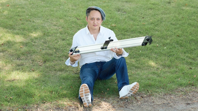 カートピア SUBARU純正アクセサリーのサイクルボードを持って芝生に座る須崎兼則さん | SUBARU