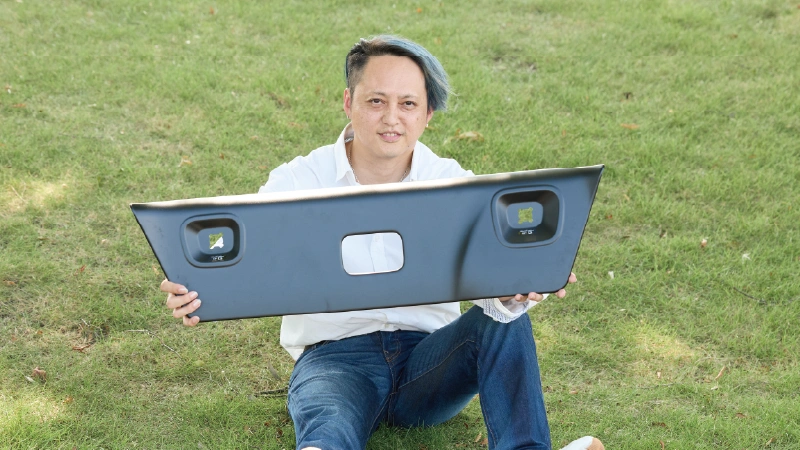 カートピア フォレスター専用の純正アクセサリー、ルーフトリムプロテクターを持って芝生に座る須崎兼則さん | SUBARU