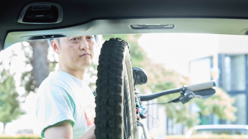 カートピア フォレスターX-BREAKのゲートを開けてマウンテンバイクを積み込んでいる様子。専用のSUBARU純正アクセサリー、ルーフトリムプロテクターに自転車の後輪が当たりそう。 | SUBARU