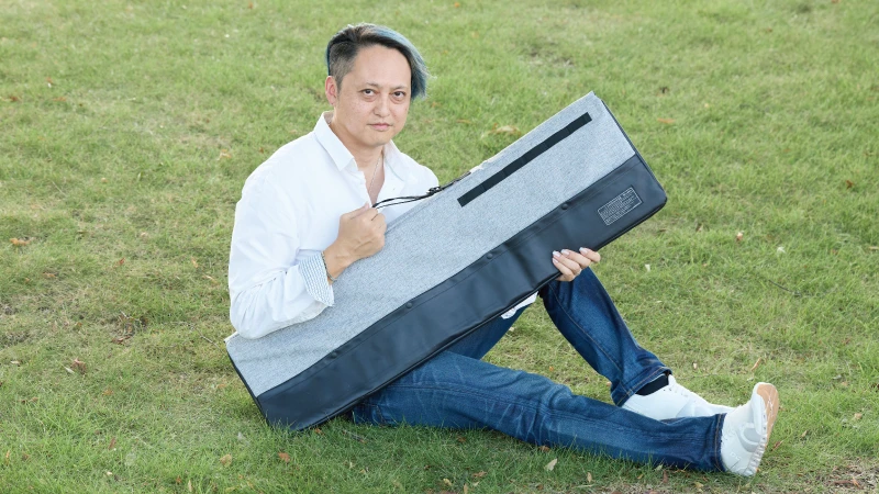 カートピア SUBARU純正アクセサリー、カーゴベンチシートを持って芝生に座る須崎兼則さん | SUBARU