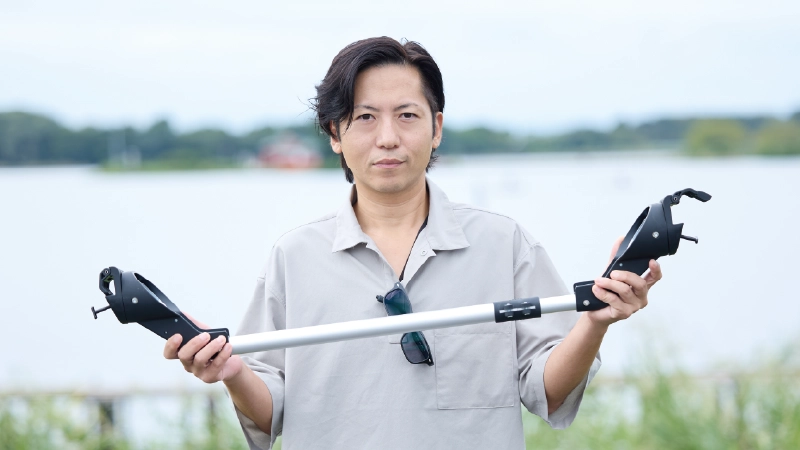 カートピア フォレスターの純正アクセサリー「ロッドホルダー」に含まれるスマートバーを手に持っているスバル用品(株)の室井さん | SUBARU