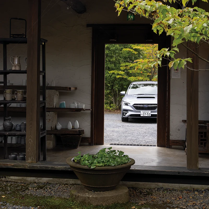 カートピア 笠間の回廊ギャラリー門の中庭から駐車場に停まっているレヴォーグGT-H EX（アイスシルバー・メタリック）を眺める様子 | SUBARU