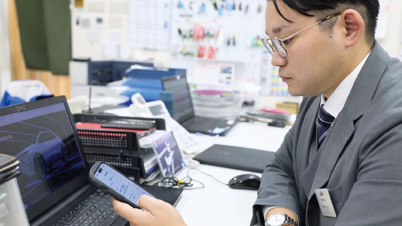 カートピア スマートフォンでアプリを確認する青島さん。 | SUBARU