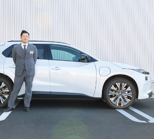 カートピア ソルテラ(ボディーカラーはプラチナホワイトパールマイカ)の横に立つ静岡スバルのセールス・青島さん。 | SUBARU