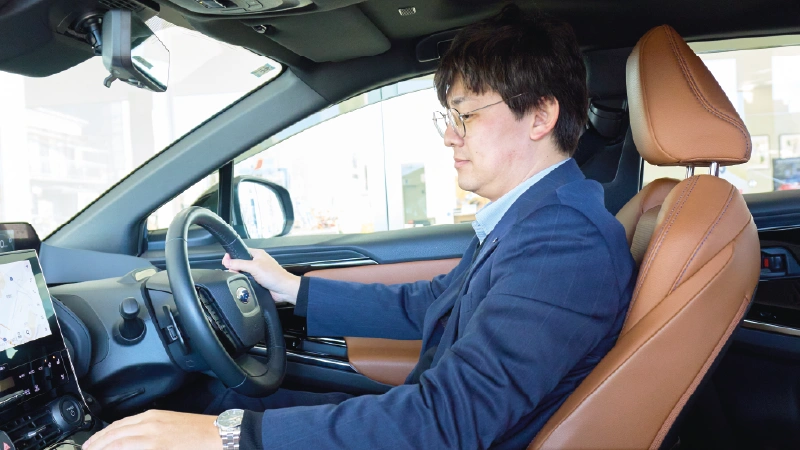 カートピア ソルテラの車内。運転席に座り、ステアリングを右手で握りながら、左手でシフトレバーなどを操作する栃木スバルのセールス・清水さん。 | SUBARU