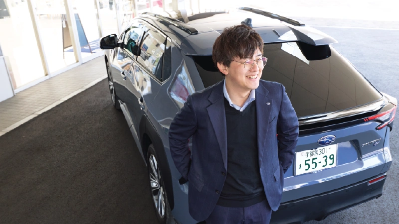 カートピア ソルテラ(ボディーカラーはハーバーミストグレーパール)のリヤ側に立つ、栃木スバルのセールス・清水さん。 | SUBARU