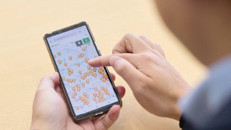 カートピア 男性が操作するスマートフォンの画面。地図が表示されており、地図上には複数のオレンジ色のピンが表示されている。 | SUBARU