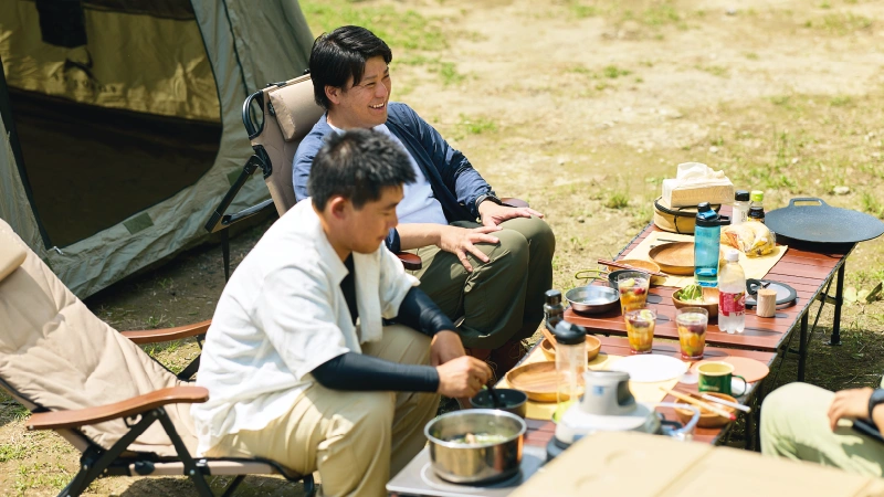 カートピア キャンプサイトのテーブルを囲み、食事をしながら話す山本さんと加藤さん | SUBARU