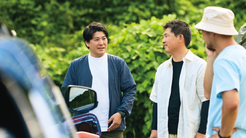 カートピア キャンプ場でトレイルシーカーのそばに立ち、会話する山本さん、加藤さん、辻榮さん。 | SUBARU